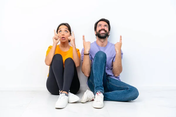 Jovem Casal Caucasiano Sentado Chão Isolado Fundo Branco Apontando Para — Fotografia de Stock