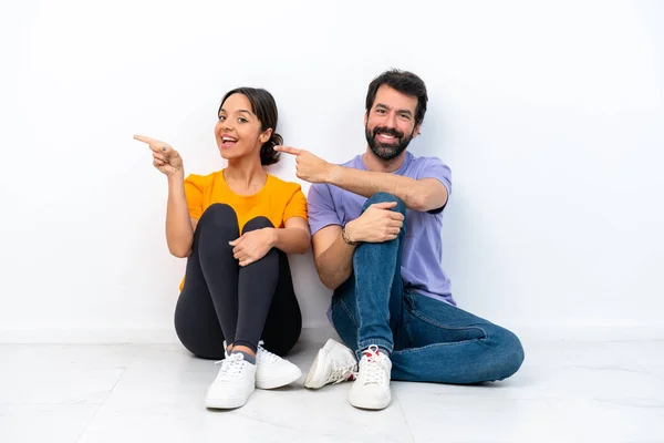Young Caucasian Couple Sitting Floor Isolated White Background Pointing Finger — Foto de Stock