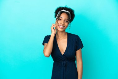 Mavi arka planda yalnız yaşayan genç Latin kadın gülüyor.