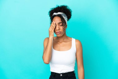 Mavi arka planda başağrısı olan genç Latin bir kadın.