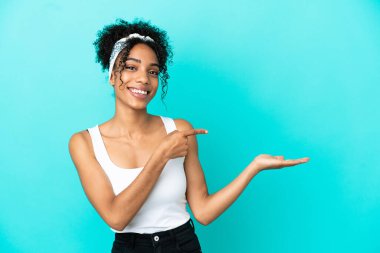 Mavi arka planda izole edilmiş genç Latin bir kadın bir ilan vermek için avucunun içinde hayali bir alan tutuyor.