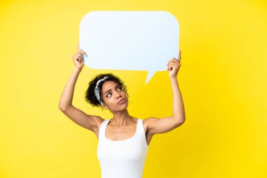Genç Afrikalı Amerikalı kadın sarı arka planda izole edilmiş boş bir konuşma balonu tutuyor ve üzgün bir ifadeyle