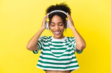 Sarı arka planda izole edilmiş genç Afrikalı Amerikalı kadın müzik dinliyor.