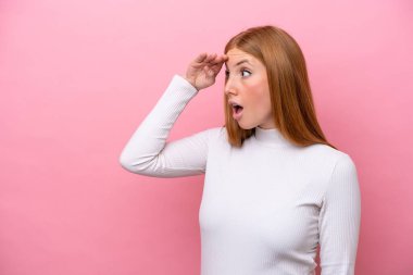 Pembe arka planda izole edilmiş genç, kızıl saçlı bir kadın.