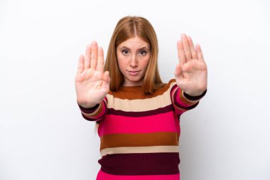 Beyaz arka planda izole edilmiş genç kızıl saçlı kadın dur hareketi yapıyor ve hayal kırıklığına uğruyor.