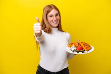 Sarı arka planda gözleme tutan genç kızıl saçlı kadın. Başparmakları havada. Çünkü iyi bir şey oldu.