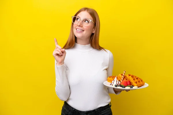 Young Redhead Woman Holding Waffles Isolated Yellow Background Pointing Great — Stock Photo, Image
