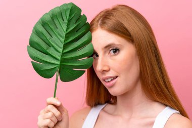 Pembe arka planda, elinde palmiye yaprağı olan genç, kızıl saçlı bir kadın. Portreyi kapat