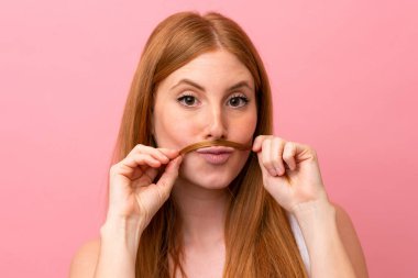 Genç kızıl saçlı kadın pembe arka planda izole edilmiş saçlarına dokunuyor. Portreyi kapat