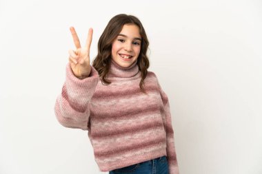 Beyaz arka planda izole edilmiş küçük beyaz kız gülümsüyor ve zafer işareti gösteriyor.