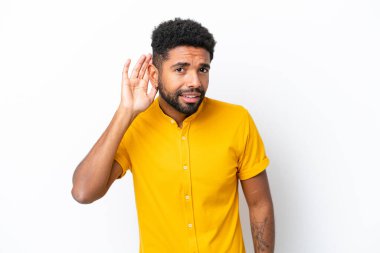 Genç Brezilyalı bir adam beyaz arka planda izole edilmiş bir şekilde elini kulağına koyarak bir şeyler dinliyor.