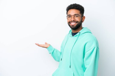 Beyaz arka planda izole edilmiş genç Brezilyalı adam, davet etmek için ellerini yana uzatıyor.