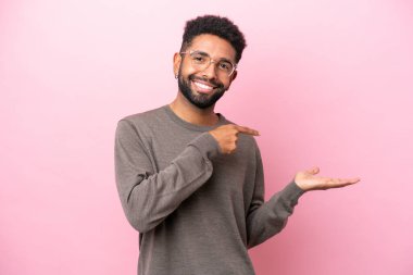 Pembe arka planda izole edilmiş genç Brezilyalı bir adam bir ilan vermek için avucunda hayali bir şey tutuyor.