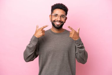 Pembe arka planda izole edilmiş genç Brezilyalı adam baş parmak hareketi yapıyor.