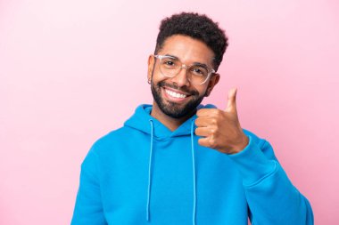 Pembe arka planda gözlüklü ve başparmağıyla izole edilmiş genç Brezilyalı bir adam.