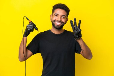 Dövmeli adam Brezilyalı izole edilmiş sarı arka planda mutlu ve parmaklarıyla üçe kadar sayıyor.