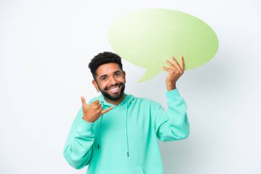 Beyaz arka planda izole edilmiş genç Brezilyalı bir adam boş bir konuşma balonu tutuyor ve telefon jesti yapıyor.