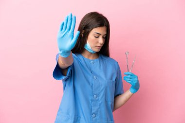 Pembe arka planda izole edilmiş aletleri tutan dişçi kadın dur hareketi yapıyor ve hayal kırıklığına uğruyor