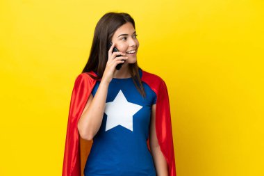 Süper kahraman Brezilyalı kadın sarı arka planda izole edilmiş cep telefonuyla biriyle sohbet ediyor.