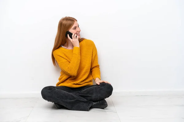 白い背景に隔離された床に座っている若い赤毛の女性誰かと携帯電話との会話を保ちます — ストック写真