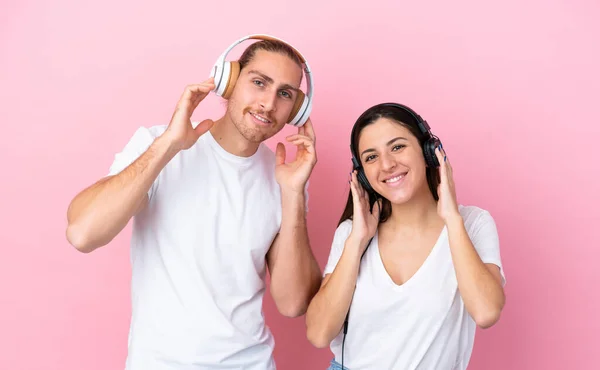 Młody Biały Para Odizolowany Różowy Tło Słuchanie Muzyka — Zdjęcie stockowe