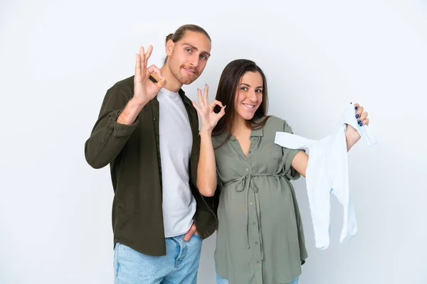 Jovem Casal Caucasiano Isolado Fundo Branco Grávida Segurando Roupas Bebê — Fotografia de Stock