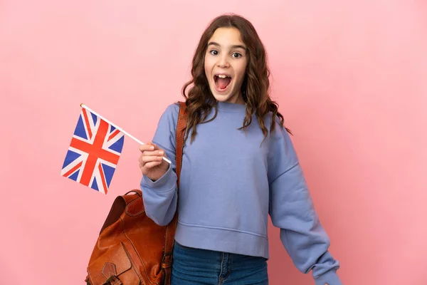一个小女孩拿着一面英国国旗 背景是粉色的 脸上露出惊讶的表情 — 图库照片
