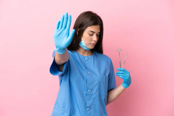牙科医生女人拿着用粉红背景隔离的工具做停止手势和失望 — 图库照片