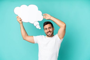 Genç, yakışıklı, beyaz bir adam mavi arka planda izole edilmiş. Elinde bir konuşma balonu var.