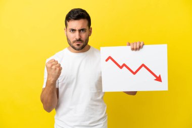 Sarı arka planda izole edilmiş yakışıklı beyaz bir adam elinde azalan bir istatistik oku sembolü ve kızgın bir levha tutuyor.