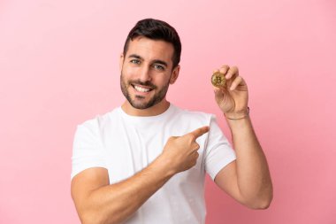 Pembe arka planda izole edilmiş Bitcoin tutan genç adam