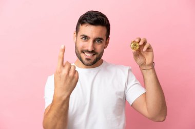 Elinde pembe arka planda izole edilmiş Bitcoin tutan genç adam geliyor.