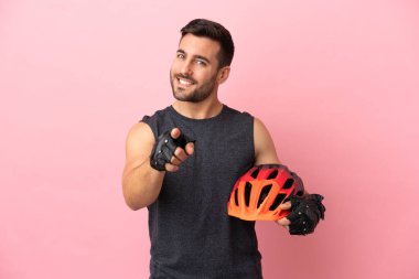 Pembe arka planda izole edilmiş genç bisikletçi mutlu bir ifadeyle ön tarafı işaret ediyor.