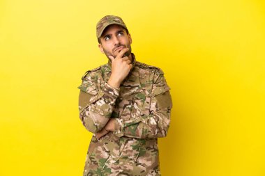 Sarı arka planda izole edilmiş askerin şüpheleri ve kafası karışmış yüz ifadesi var.