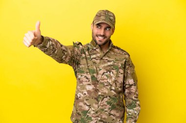 Asker sarı arka planda izole edilmiş bir şekilde baş parmak işareti yapıyor.