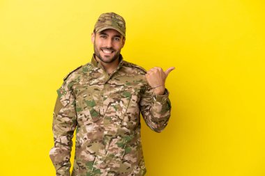 Sarı arka planda izole edilmiş bir asker bir ürün sunmak için kenarı işaret ediyor.