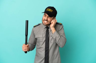 Mavi arka planda izole edilmiş genç güvenlik görevlisi hayal kırıklığına uğramış ve kulaklarını kapatmış.