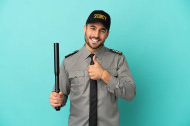 Genç güvenlik görevlisi mavi arka planda izole edilmiş bir şekilde baş parmak işareti yapıyor.