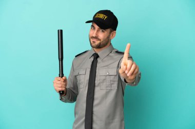 Mavi arka planda izole edilmiş genç güvenlik görevlisi parmağını kaldırıyor ve gösteriyor.