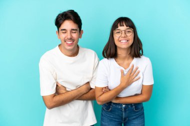 Mavi arka planda soyutlanmış genç melez çift gülümserken kollarını kavuşturuyor.