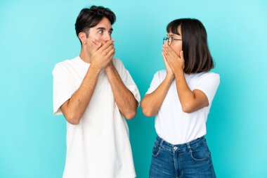 Genç melez çift, mavi arka planda izole edilmiş ağızlarını uygunsuz bir şey söyledikleri için elleriyle kapatıyor.
