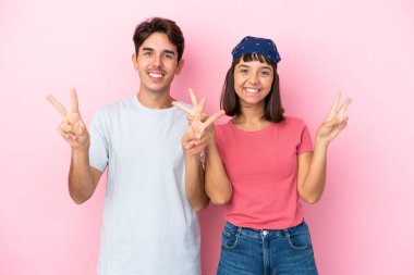 Pembe arka planda izole edilmiş genç bir çift gülümsüyor ve zafer işareti gösteriyorlar.