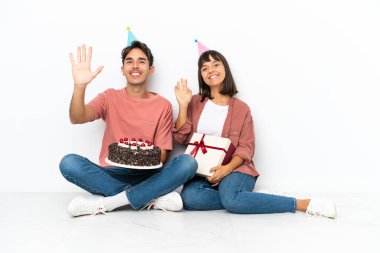 Genç melez bir çift, doğum gününü kutluyor. Beyaz arka planda izole bir şekilde, mutlu bir ifadeyle selamlıyorlar.