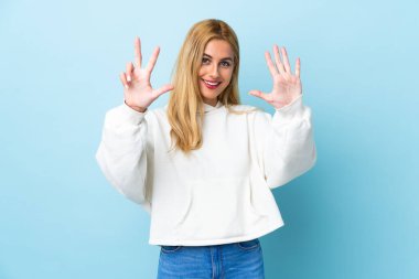 Genç Uruguaylı sarışın kadın izole edilmiş mavi arka planda sekiz parmaklı sayıyor.