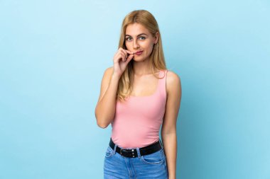 Genç Uruguaylı sarışın kadın izole edilmiş mavi arka planda sessizlik işareti gösteriyor.