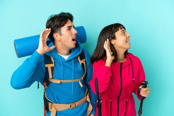 Pareja Jóvenes Montañeros Aislados Sobre Fondo Azul Escuchando Algo Poniendo —  Fotos de Stock