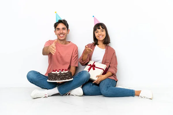 一对年轻的混血种族夫妇坐在地板上庆祝生日 他们与白人背景的人握手以庆祝他们的生日 — 图库照片