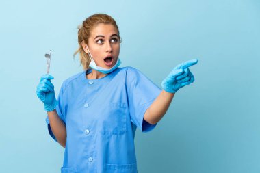 İzole edilmiş mavi arka plan üzerinde aletleri tutan genç bir dişçi.