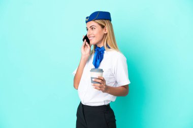Uçak hostesi Uruguaylı kadın mavi arka planda izole edilmiş. Elinde kahve ve cep telefonu var.