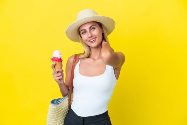 Sarışın Uruguaylı yaz kızı elinde dondurmayla sarı arka planda izole edilmiş kahkahalar atıyor.